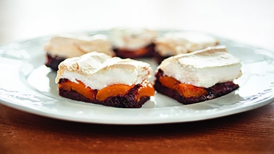 Vier Desserttafeln mit einem Schokoladenboden, einer Schicht aus Orangenfrüchten und einem fluffigen, gerösteten Baiser-Topping sind auf einem weißen Teller angeordnet.