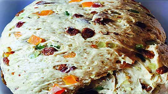 Nahaufnahme eines Teigs mit bunten kandierten Früchten und Rosinen, bereit zum Backen.