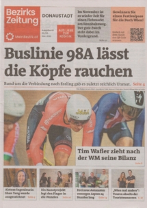 Titelseite einer deutschsprachigen Zeitung mit der Hauptschlagzeile Buslinie 98A lässt die Köpfe rauchen und einem großen Foto von Radfahrern bei einem Rennen. Kleinere Schlagzeilen und Artikel umgeben das Hauptbild.