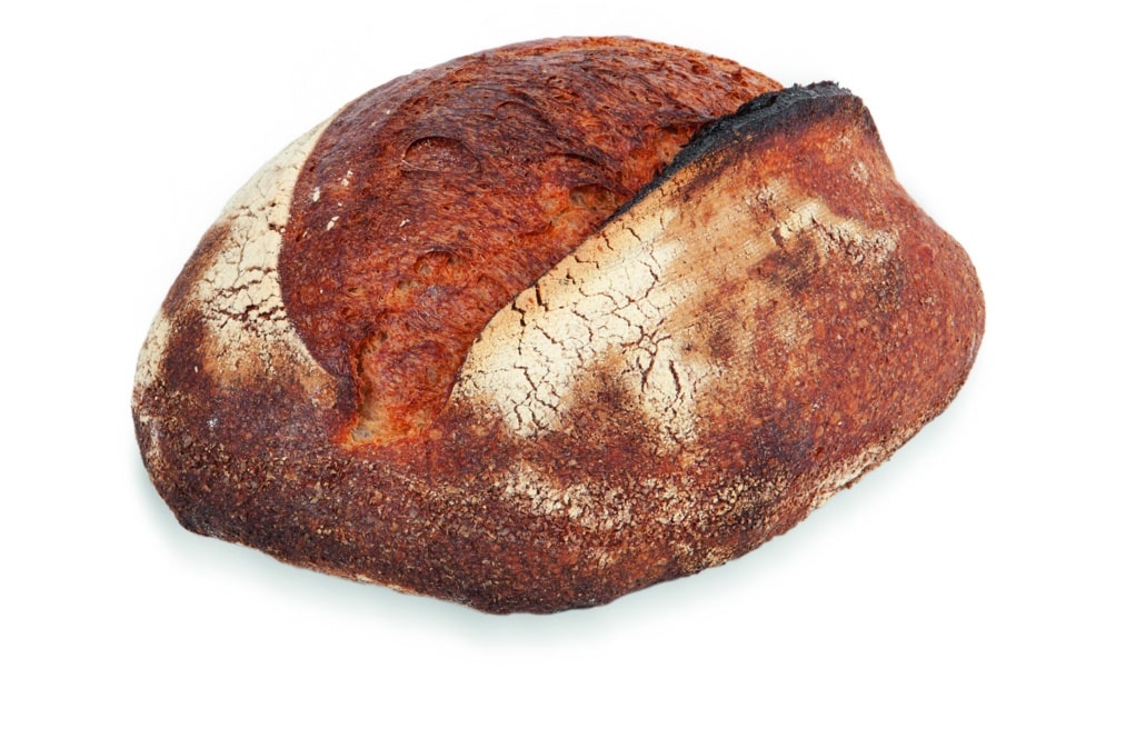 Ein runder, rustikaler, handwerklich hergestellter Brotlaib mit einer dunklen, knusprigen Außenseite und einer gespaltenen Oberseite auf einem weißen Hintergrund.