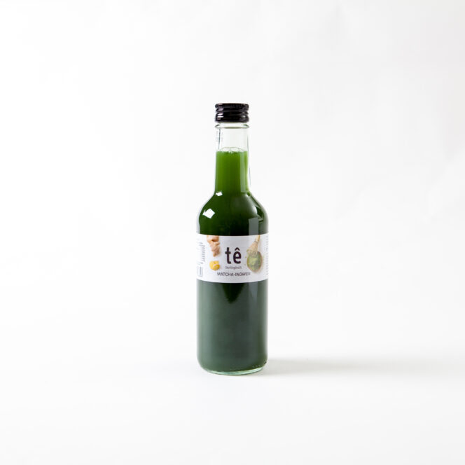 Eine mit grüner Flüssigkeit gefüllte Klarglasflasche mit schwarzem Verschluss und weißem Etikett mit der Aufschrift tê und matcha bowlito auf weißem Hintergrund.