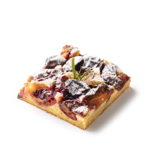Ein quadratisches Stück Pflaumenkuchen mit Puderzucker und einer kleinen grünen Garnierung auf weißem Hintergrund.