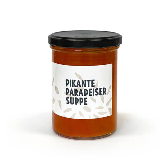 Ein Glasgefäß mit schwarzem Deckel, das rote Suppe enthält. Auf dem Etikett steht Pikante Paradeiser Suppe mit einem einfachen Samenmuster um den Text herum.