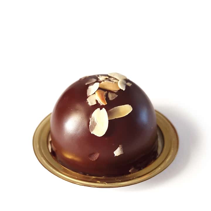 Ein kuppelförmiges Schokoladendessert auf einem goldenen Boden, belegt mit dünn geschnittenen Mandeln, auf weißem Hintergrund.