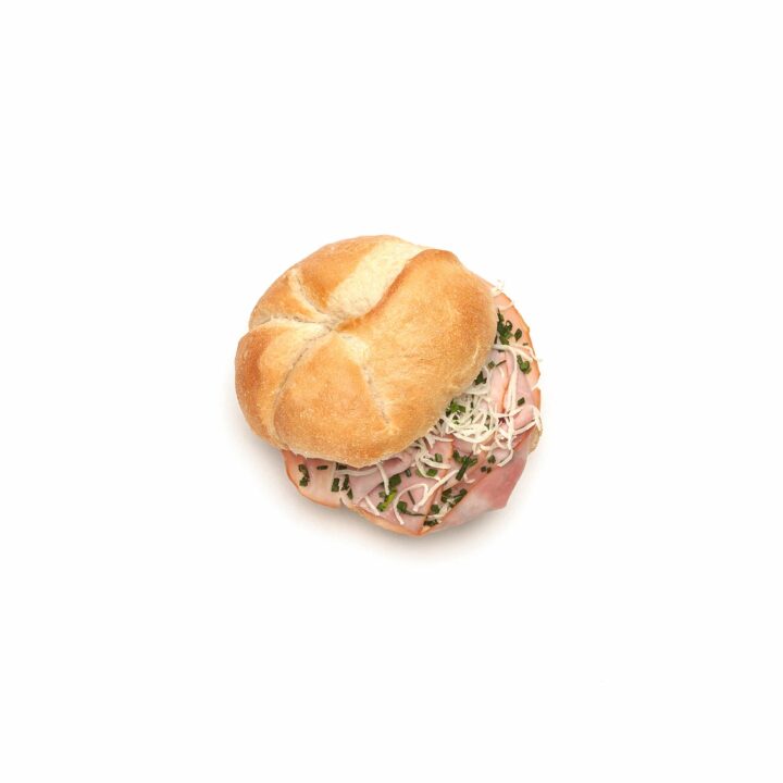 Ein rundes Sandwichbrötchen, gefüllt mit geschnittenem Fleisch, geraspeltem Salat und Sprossen, fotografiert auf einem einfachen weißen Hintergrund.