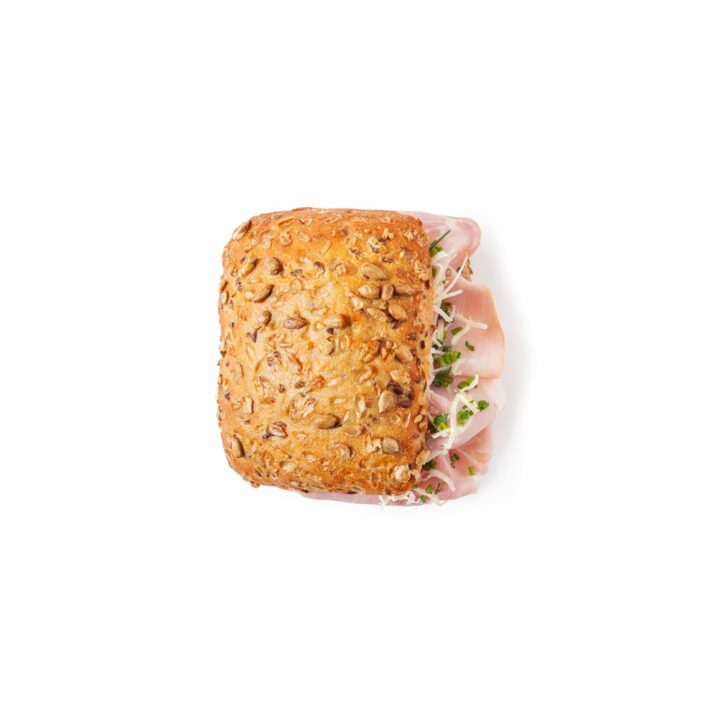 Ein entkörntes Vollkornbrötchen, gefüllt mit Schinkenscheiben und geraspeltem Salat, fotografiert von oben auf weißem Hintergrund.