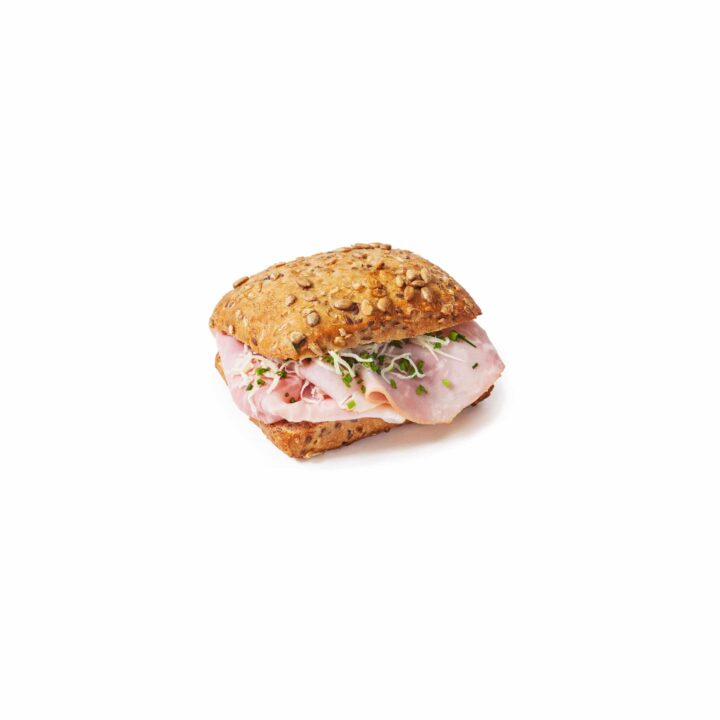 Ein Mehrkornbrötchen, gefüllt mit Schinkenscheiben, Käse und frischen Sprossen, vor einem schlichten weißen Hintergrund.