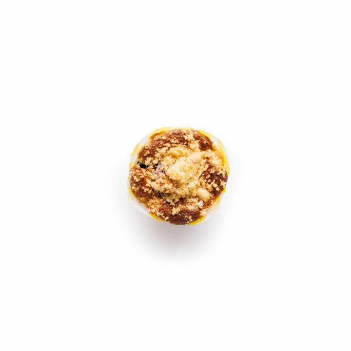 Ein einzelner Muffin mit Streuselbelag befindet sich in der Mitte eines einfarbig weißen Hintergrunds.