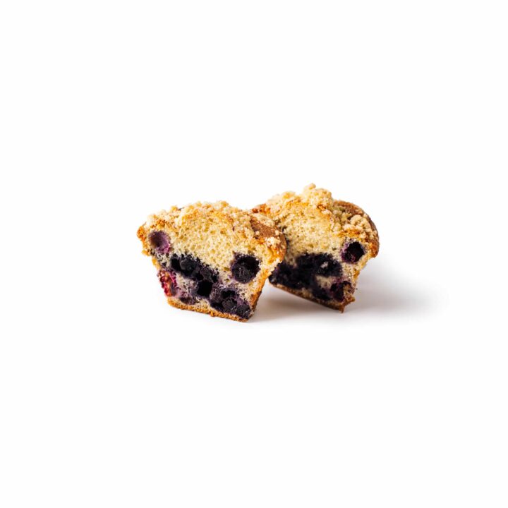 Ein halbierter Blaubeermuffin mit goldbraunem Äußeren und einem mit ganzen Blaubeeren gefüllten Inneren auf einem weißen Hintergrund.