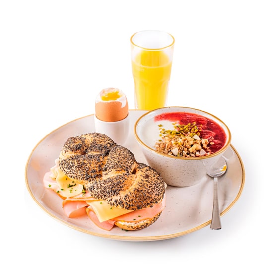 Ein Teller mit einem belegten Sandwich mit Schinken und Käse, einem weichgekochten Ei, einer Schüssel Joghurt mit Müsli und Fruchtsauce, einem Löffel und einem Glas Orangensaft, alles auf weißem Hintergrund.