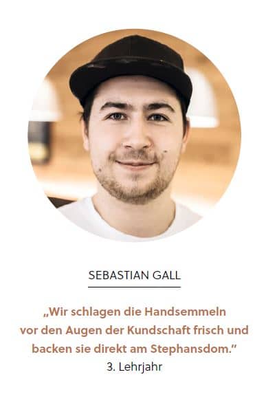 Ein junger Mann mit einer schwarzen Mütze und einem weißen Hemd lächelt in die Kamera. Darunter steht der Name Sebastian Gall und ein Zitat auf Deutsch über das Backen von frischen Brötchen vor den Augen der Kunden. 3. Lehrjahr zeigt sein drittes Lehrjahr an.