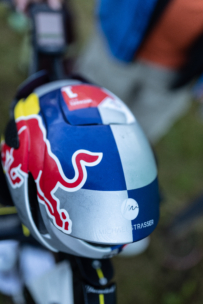 Nahaufnahme eines Fahrradhelms mit dem Red Bull-Logo und dem Namen Michael Strasser auf blauem, silbernem und rotem Design, mit unscharfem Außenhintergrund.