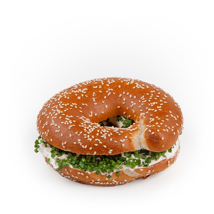 Ein mit Frischkäse und Schnittlauch gefülltes Sesam-Bagel-Sandwich vor einem schlichten weißen Hintergrund.
