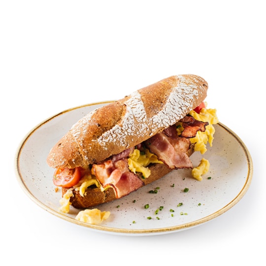 Ein rustikales Brötchen, gefüllt mit Rührei, knusprigem Speck und halbierten Kirschtomaten, serviert auf einem weißen Teller mit gehacktem Schnittlauch.