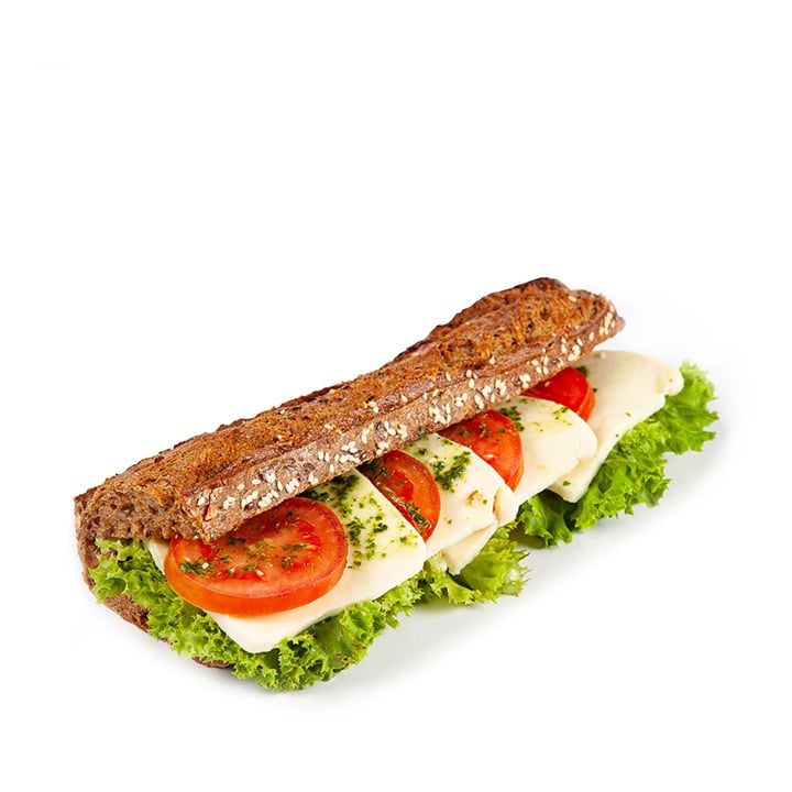 Ein Vollkorn-Baguette-Sandwich, gefüllt mit Blattsalat, Tomatenscheiben, Mozzarella-Käse und Kräutern, vor weißem Hintergrund.