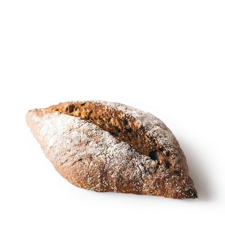 Ein rustikaler, ovaler Laib Vollkornbrot mit etwas Mehl auf der Oberseite, isoliert auf einem weißen Hintergrund.