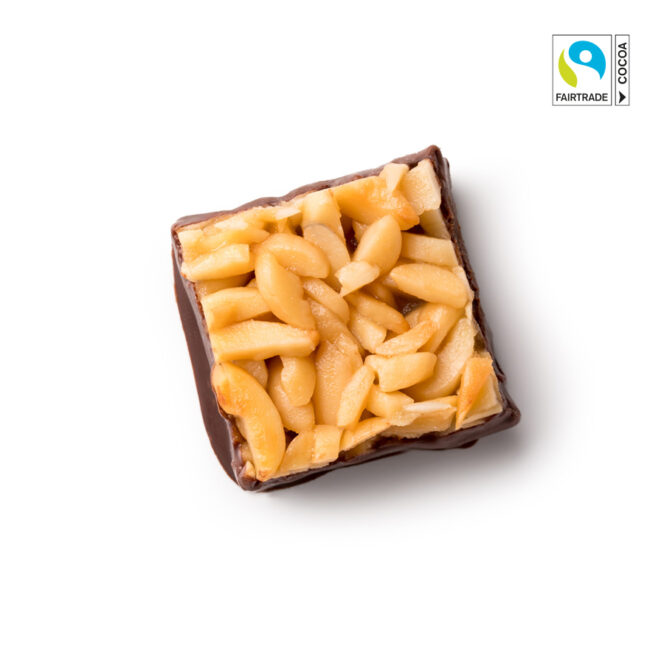 Ein quadratischer Schokoladengenuss mit gehackten Mandeln auf weißem Hintergrund. In der rechten oberen Ecke ist das Logo der Fairtrade-Kakao-Zertifizierung zu sehen.