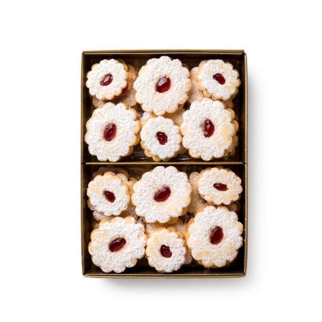 Eine Schachtel mit zwölf runden, mit Puderzucker bestäubten und in der Mitte mit roter Marmelade gefüllten Sandwich-Keksen, die ordentlich in zwei Reihen angeordnet sind.