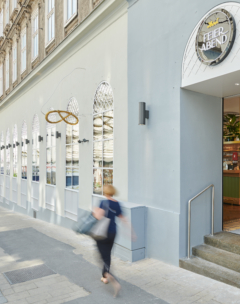 Eine verschwommene Person geht am Eingang eines modernen Restaurants namens Feier Abend mit großen Bogenfenstern und hellblau-grauen Wänden in einer Stadtstraße vorbei.