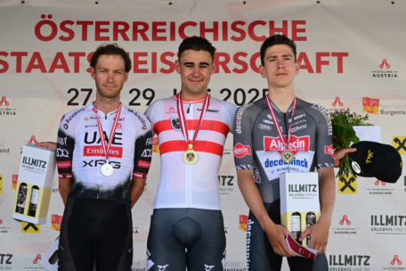 Drei männliche Radsportler mit Medaillen stehen bei den österreichischen Staatsmeisterschaften auf einem Podium und halten Preise in der Hand.