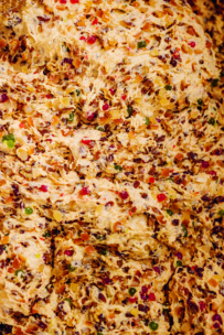 Nahaufnahme von Obstkuchenteig mit gemischten bunten kandierten Früchten, Nüssen und Teig, die ein strukturiertes und lebendiges Aussehen erzeugen.