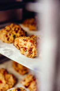 Nahaufnahme eines ungebackenen Brotteigs mit Früchten und Nüssen auf einem bemehlten Backblech, bereit zum Backen im Ofen. Der Teig enthält sichtbare Stücke von Trockenfrüchten und Nüssen.