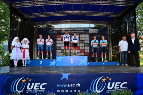Die Radsportteams stehen bei den UEC-Europameisterschaften im Bahnradsport auf dem Siegerpodest mit den Gold-, Silber- und Bronzemedaillengewinnern. Offizielle und Frauen in traditionellen Kostümen stehen auf beiden Seiten der Bühne.