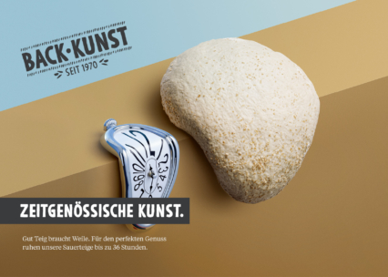 Ein runder Brotlaib liegt neben einer schmelzenden Uhr, die von Salvador Dalí inspiriert wurde. Der Text lautet: "BACK-KUNST seit 1970" und "Zeitgenössische Kunst". Ein zusätzlicher deutscher Text beschreibt das Verfahren der Sauerteig-Rastung.