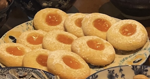 Ein Teller mit runden, mit Orangenmarmelade bestrichenen und mit Puderzucker bestäubten Plätzchen steht zwischen dekorativen Schalen.