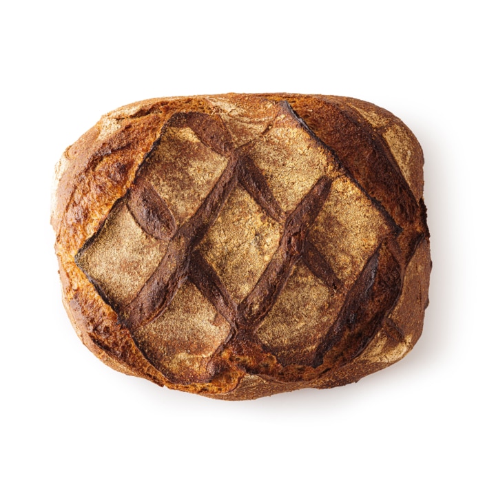 Ein runder, handwerklich hergestellter Brotlaib mit goldbrauner Kruste und einem kreuzförmigen Muster auf der Oberseite, fotografiert auf weißem Hintergrund.