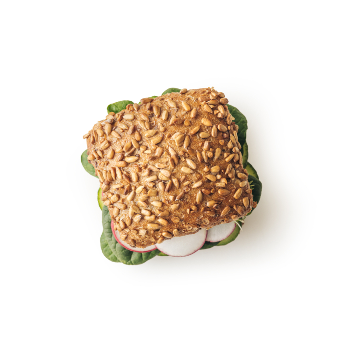 Ein Sandwich aus einem quadratischen Mehrkornbrötchen, belegt mit Sonnenblumenkernen, gefüllt mit Blattgemüse und Radieschenscheiben, von oben gesehen auf weißem Hintergrund.