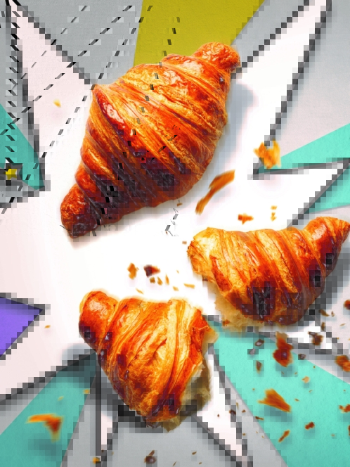 Drei goldene Croissants, von denen eines in der Mitte zerbrochen und mit Krümeln übersät ist, ruhen auf einem farbenfrohen Hintergrund im Comic-Stil mit kühnen Linien und Sternschnuppen.