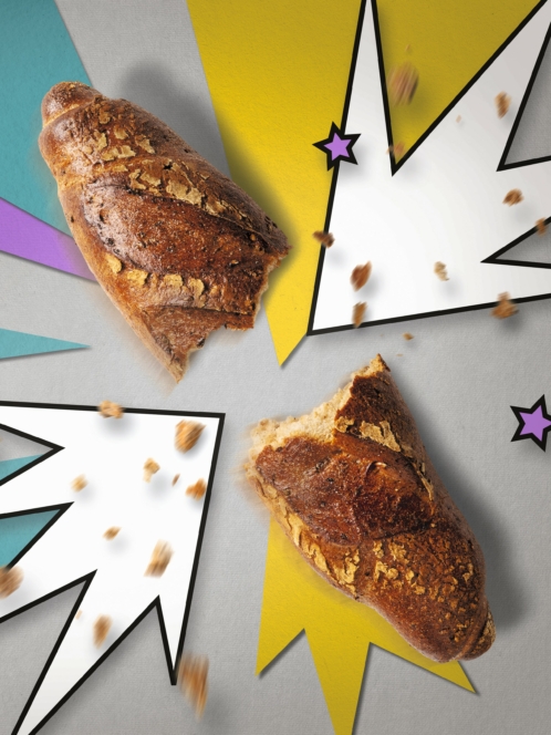 Zwei knusprige Brotstücke brechen auseinander, während im Hintergrund illustrierte, comicartige Ausbrüche und Sterne zu sehen sind und Krümel umherfliegen, was einen dynamischen und spielerischen Effekt erzeugt.
