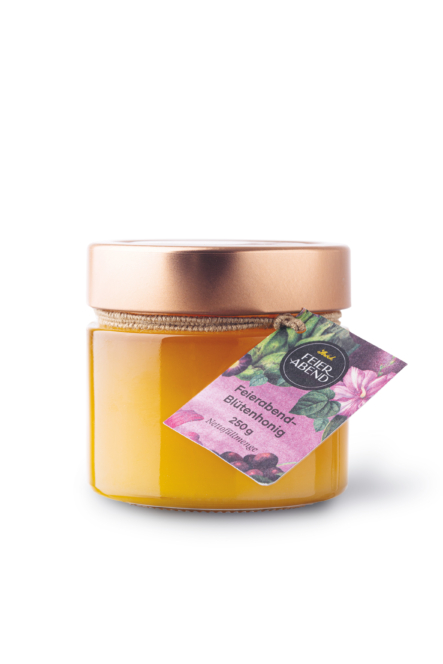 Ein mit gelbem Honig gefülltes Glas, das mit einem goldenen Metalldeckel verschlossen und mit einem farbenfrohen Etikett und Anhänger mit Blumenmotiven und Text verziert ist.