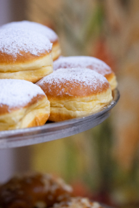 Nahaufnahme mehrerer runder, goldbrauner, mit Puderzucker bestäubter Donuts, die auf einem Metalltablett vor einem unscharfen, bunten Hintergrund präsentiert werden.