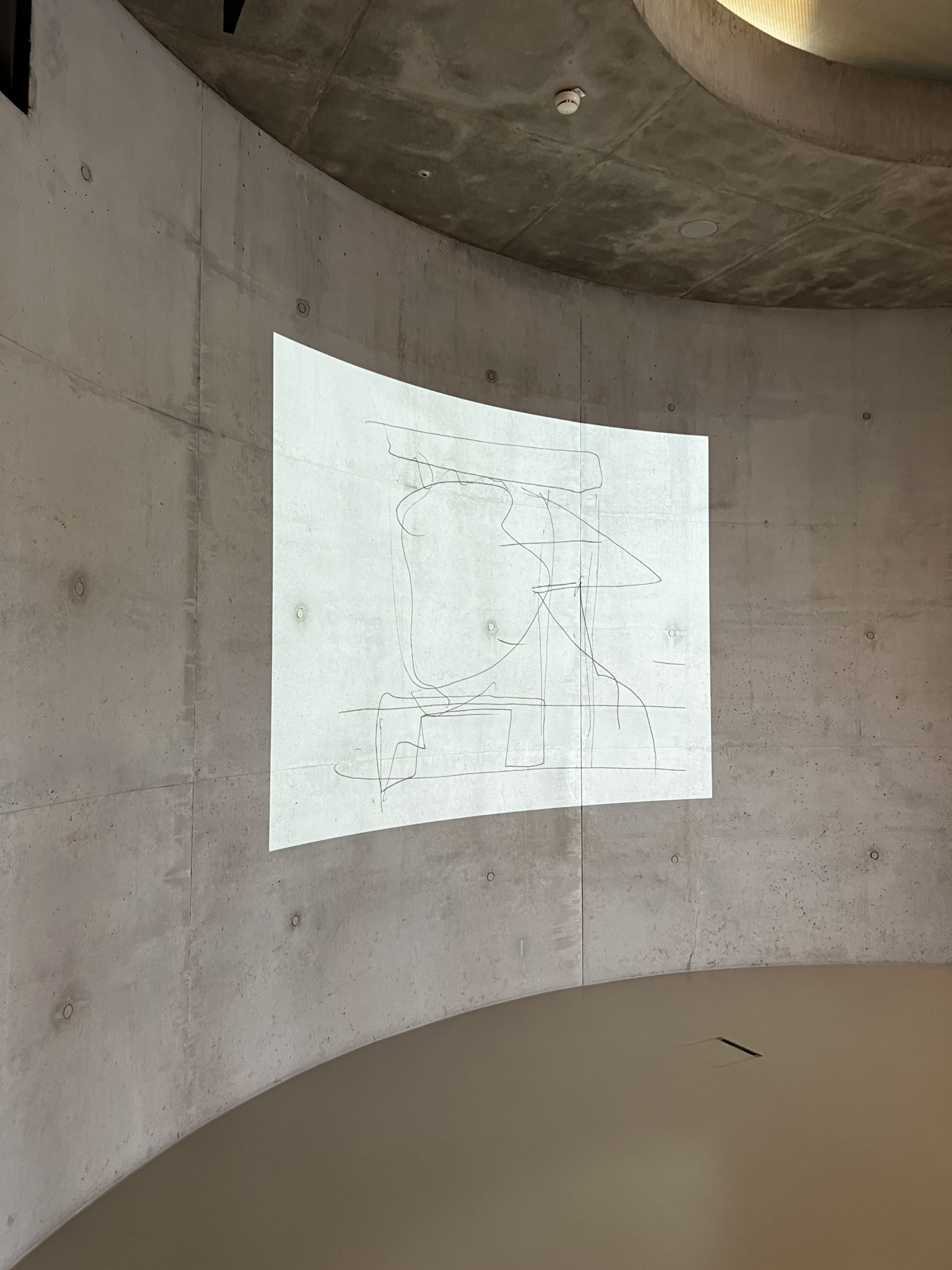 Eine minimalistische Linienzeichnung wird auf eine gebogene Betonwand in einem modernen, leeren Raum projiziert. Das Kunstwerk erscheint abstrakt, wobei sich kreuzende Linien eine undefinierte Figur oder Form bilden.
