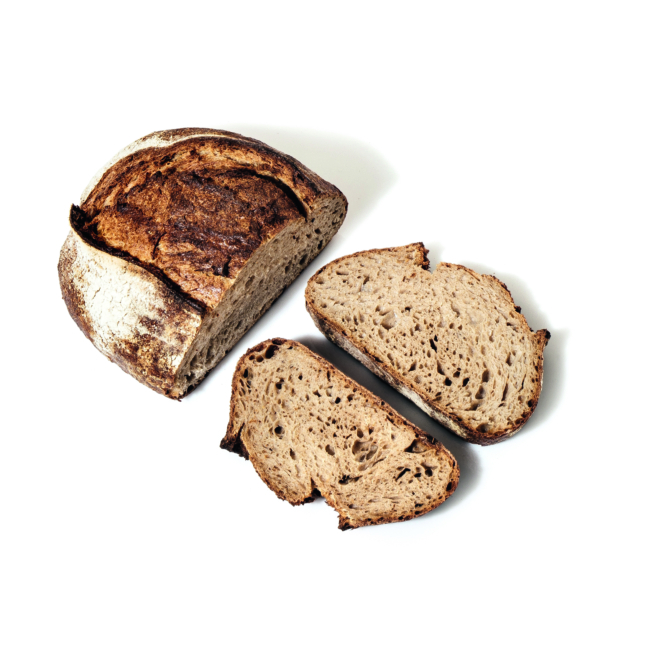 Ein rustikaler runder Laib Schwarzbrot mit dunkler Kruste liegt neben zwei dicken Scheiben auf weißem Hintergrund.