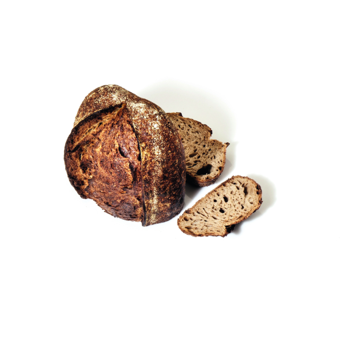 Ein runder Laib rustikales, knuspriges Schwarzbrot mit zwei abgeschnittenen Scheiben, die daneben liegen, auf einem schlichten weißen Hintergrund.