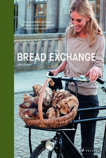 Eine lächelnde Frau steht im Freien und hält ein Fahrrad mit einem großen Korb voller rustikaler Brotlaibe in der Hand. Der Buchtitel The Bread Exchange und die Autorin Malin Elmlid sind auf dem Bild zu sehen.