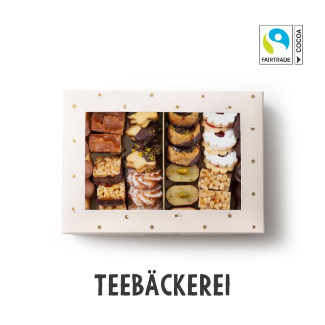 Eine Schachtel mit verschiedenen deutschen Keksen und Gebäck wird von oben betrachtet. Die Schachtel ist cremefarben und hat ein durchsichtiges Fenster. Das Fairtrade-Kakao-Logo erscheint oben rechts. Der Text darunter lautet TEEBÄCKEREI.