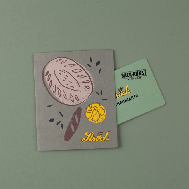 Ein grauer Kartenhalter mit einer Brotillustration und der Aufschrift "das Stück" in Gelb, mit einer grünen Mitgliedskarte, die sich teilweise im Inneren befindet, auf hellgrünem Hintergrund.