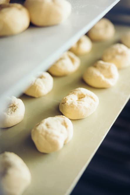 Reihen von ungebackenen Brötchen sind auf Metallblechen aufgereiht, die auf verschiedenen Ebenen eines industriellen Backgestells angeordnet sind, bereit zum Backen.