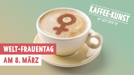 Eine Tasse Kaffee mit dem Symbol des weiblichen Geschlechts, das mit Kakaopulver auf den Schaum gezeichnet wurde. Der Text lautet: Welt-Frauentag am 8. März und Kaffee-Kunst seit 1970 auf einem pastellfarbenen Hintergrund.