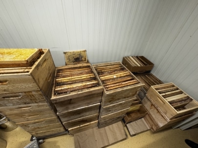 In einem Lagerraum mit hellen Wänden und hellem Fußboden stehen mehrere Stapel hölzerner Bienenkästen, teilweise mit Wabenrahmen darin.
