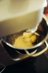 Ein Standmixer mischt den Teig in einer Edelstahlschüssel und vermengt die Zutaten zu einem glatten, dicken Teig. Das Bild ist von oben aufgenommen und zeigt die Bewegung des Mischvorgangs.