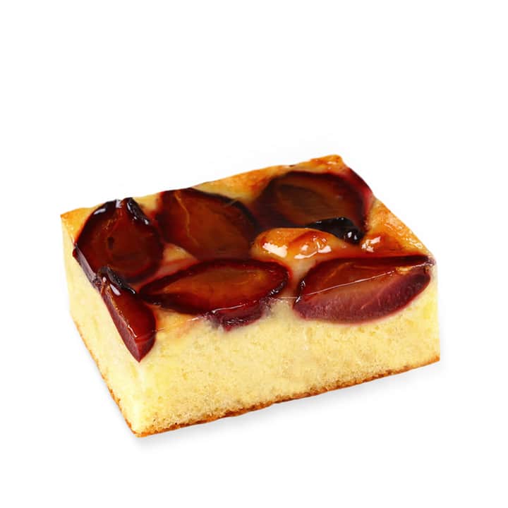 Eine rechteckige Kuchenscheibe, belegt mit halbierten Pflaumen, mit einem goldenen, fluffigen Boden und glänzenden Fruchtstücken obenauf.