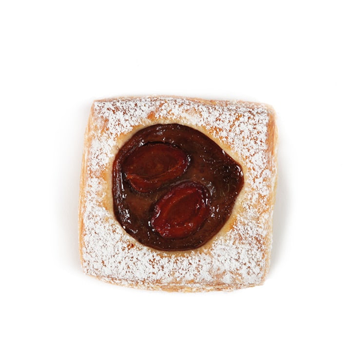 Ein quadratischer, mit Puderzucker bestreuter Blätterteig, gefüllt mit dunkler Fruchtkonfitüre, wahrscheinlich Pflaume, steht in der Mitte auf weißem Grund.