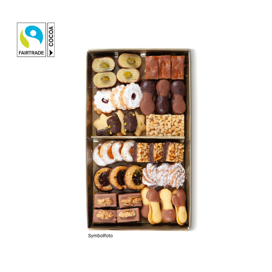 Eine Schachtel mit sortierten Keksen in verschiedenen Formen, Farben und Belägen, die in zwei Reihen angeordnet sind. Das Fairtrade-Kakao-Logo erscheint in der oberen linken Ecke. Der Hintergrund ist weiß.