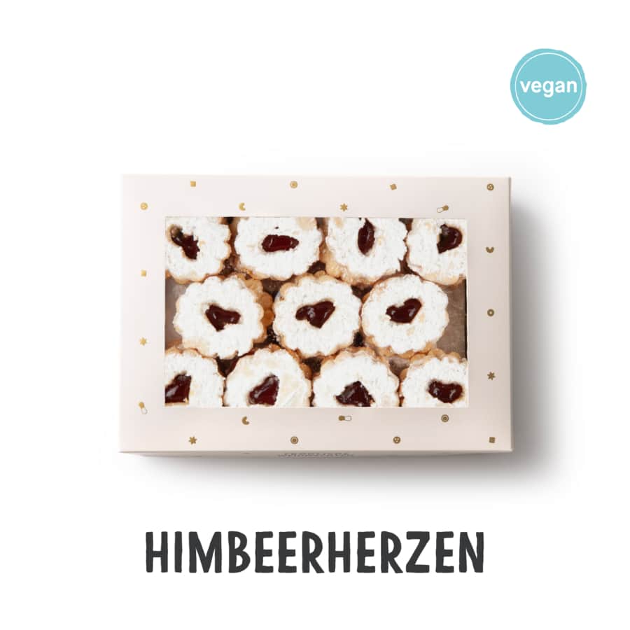 Eine Schachtel mit herzförmigen Linzer Keksen mit Himbeerfüllung und Puderzucker obenauf, von oben gesehen. Das Wort HIMBEERHERZEN und ein veganes Etikett erscheinen auf dem Bild.