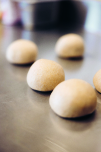 Mehrere runde Teigkugeln sind auf einer glänzenden Metallfläche angeordnet, bereit zum Backen oder Kochen. Der Hintergrund ist weich und unscharf.
